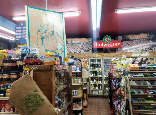 Interior of a convenience store featuring shelves of products, a Budweiser sign, and a colorful mural.