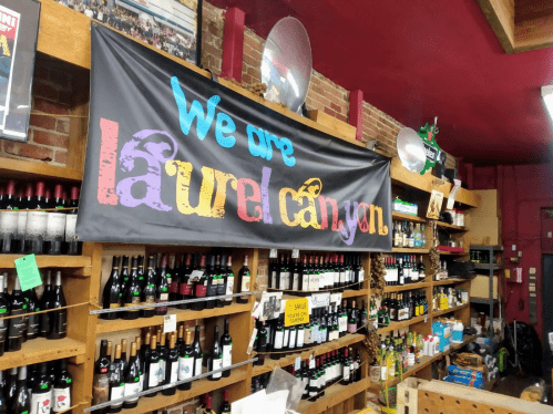 A colorful banner reading "We are Laurel Canyon" hangs above shelves filled with various wine bottles in a store.