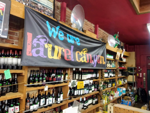 A colorful banner reading "We are Laurel Canyon" hangs above shelves filled with various wine bottles in a store.
