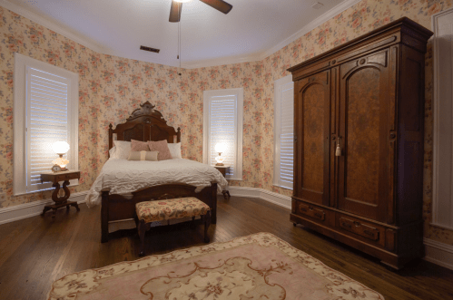 Cozy bedroom with floral wallpaper, a wooden bed, antique wardrobe, and soft lighting from bedside lamps.
