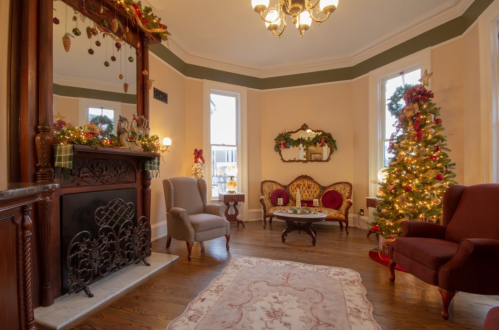 Cozy living room decorated for the holidays, featuring a Christmas tree, elegant furniture, and a fireplace.