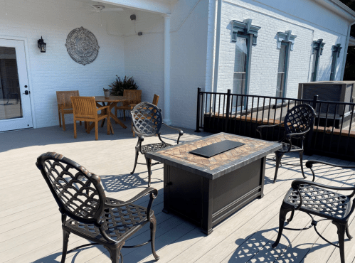 A patio with a fire pit table surrounded by four chairs and a dining table in the background.