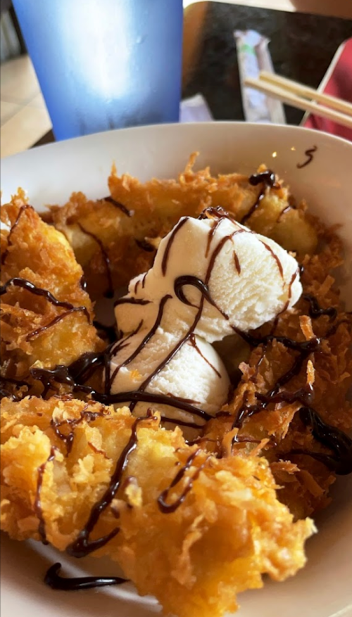 A bowl of crispy fried dessert topped with vanilla ice cream and drizzled with chocolate sauce.