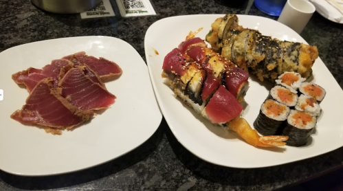 A plate with sliced tuna sashimi on the left and various sushi rolls on the right, including tempura and maki.