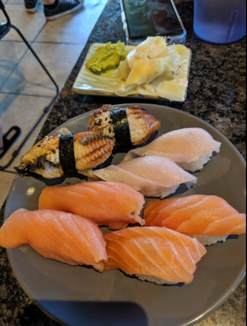 A plate of sushi featuring eel nigiri, salmon nigiri, wasabi, and pickled ginger on a black table.