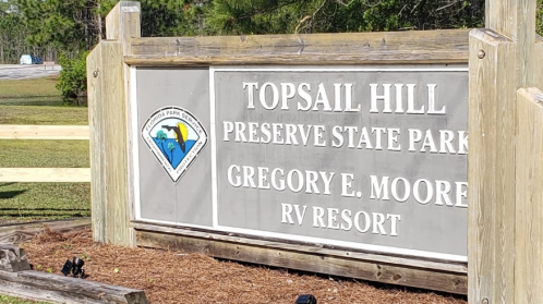 Sign for Topsail Hill Preserve State Park and Gregory E. Moore RV Resort, surrounded by greenery.