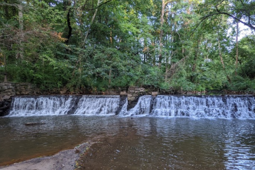 A serene waterfall cascading over rocks into a calm river, surrounded by lush green trees and foliage.
