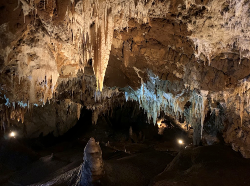 A dimly lit cave interior featuring stalactites and stalagmites, with blue lighting highlighting the formations.