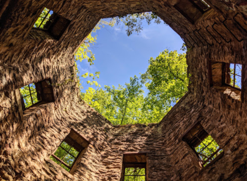 View from inside a stone structure, looking up at a blue sky and green trees through an octagonal opening.