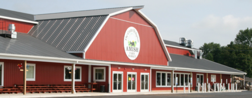 A red barn-style building with a sign reading "Amish Farm Market" and a porch with benches.