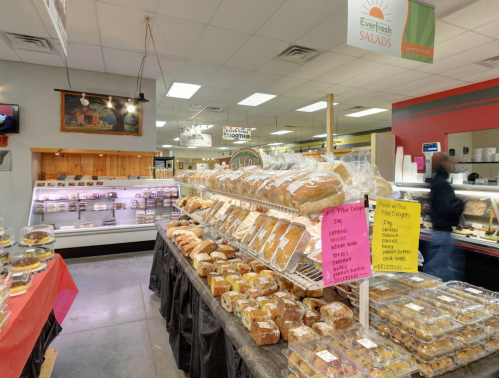 A bakery display filled with various breads and pastries in a market, with a colorful sign indicating prices.