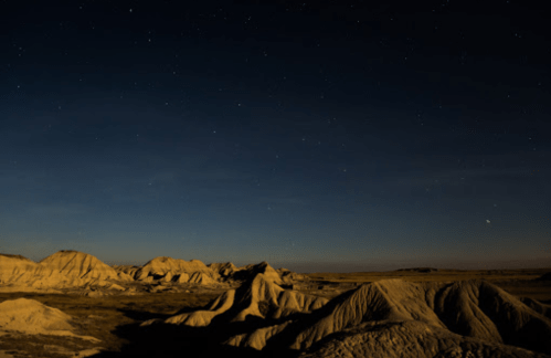 A serene night landscape with rolling hills under a starry sky, illuminated by a soft moonlight glow.