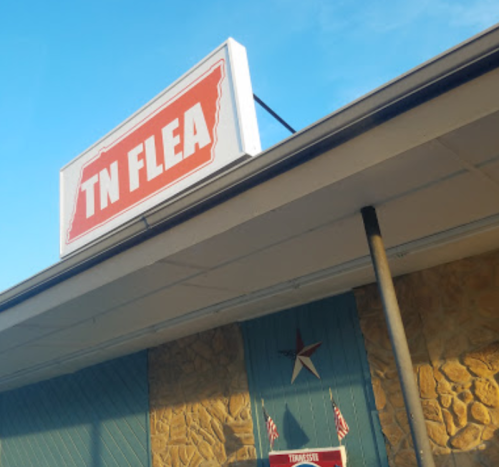 Sign for "TN FLEA" on a building with a blue sky above and a stone wall below.