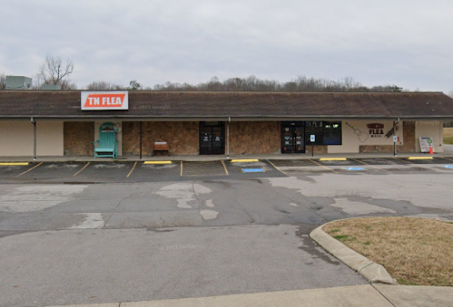 Exterior view of a flea market building with a sign reading "TN FLEA" and empty parking spaces in front.