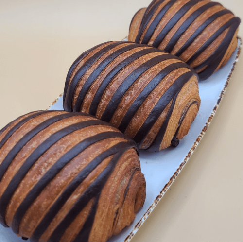Three chocolate-striped pastries arranged on a white plate, showcasing a golden-brown, flaky texture.
