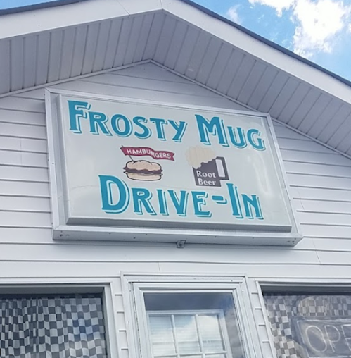 Sign for "Frosty Mug Drive-In" featuring hamburgers and root beer, with a blue sky in the background.