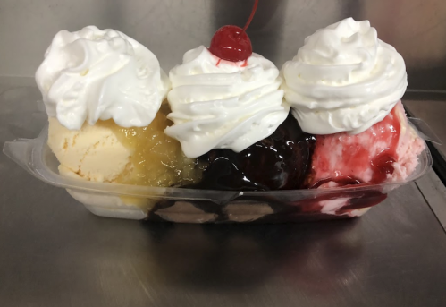 A colorful ice cream sundae with three scoops topped with whipped cream and cherries, served in a clear dish.