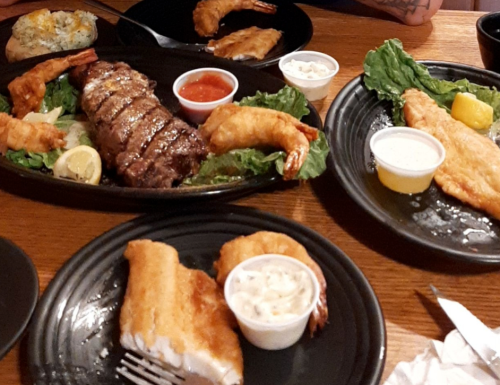 A table with two plates of seafood and steak, garnished with lettuce and sauces, ready to be enjoyed.