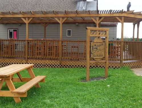 A wooden deck with a sign for "Beacon Bar & Grill" and a picnic table on a grassy area.