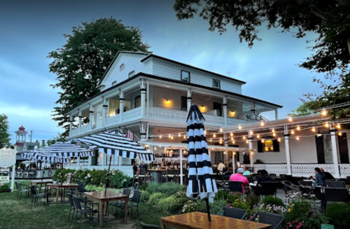 A charming restaurant with outdoor seating, striped umbrellas, and string lights, set against a twilight sky.