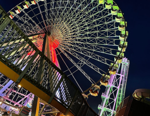 A brightly lit ferris wheel at night, with colorful lights illuminating its structure against a dark sky.