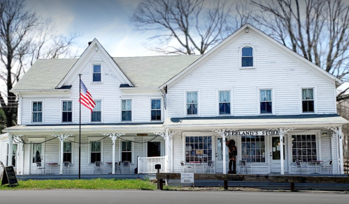 A white, two-story building with a porch, featuring an American flag and a sign for "Overland Store."