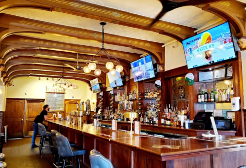 A cozy bar interior with wooden accents, multiple TVs, and a bartender preparing drinks at the counter.