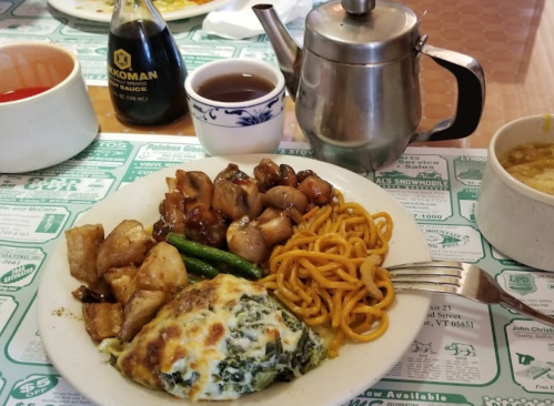 A plate of food with chicken, noodles, potatoes, green beans, and a spinach omelet, alongside a teapot and sauces.