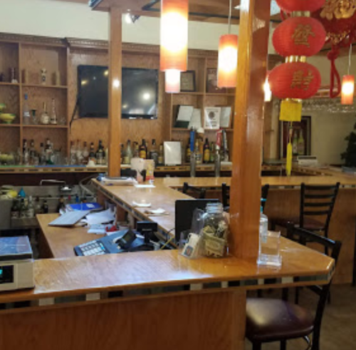 A cozy restaurant bar area with wooden decor, bottles on shelves, and red lanterns hanging from the ceiling.