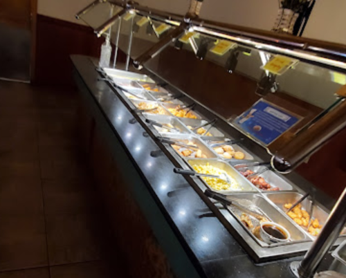 A buffet with various food trays, including meats, vegetables, and desserts, under glass covers.