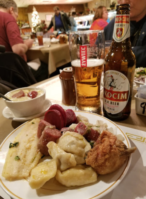 A plate of assorted foods including dumplings, sausage, and fried chicken, with a beer and soup in the background.