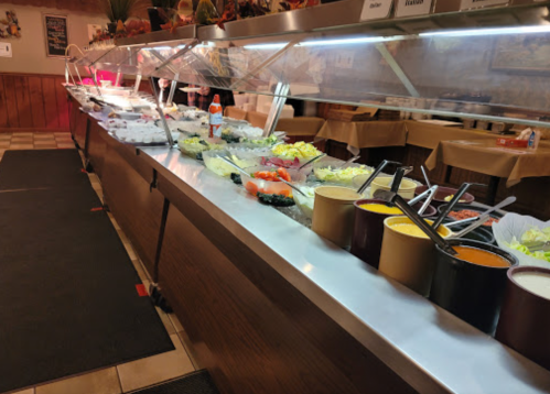 A buffet with various dishes, including salads and sauces, displayed under glass in a restaurant setting.