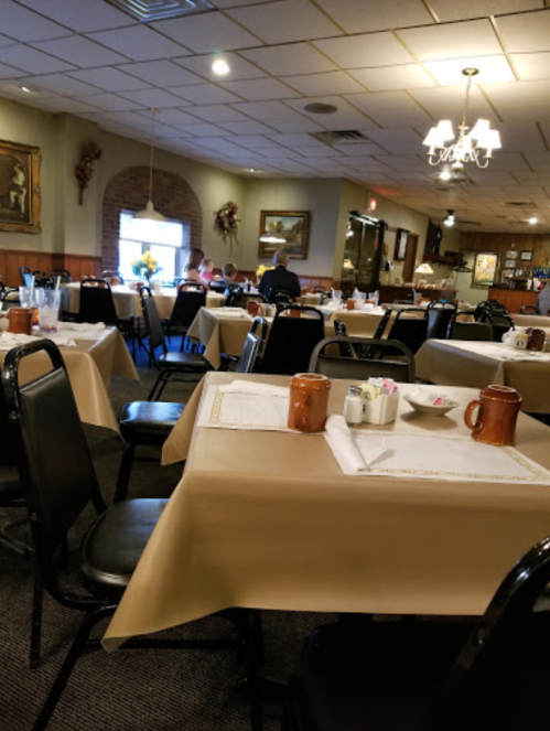 A spacious restaurant interior with empty tables set for dining, featuring beige tablecloths and a cozy atmosphere.