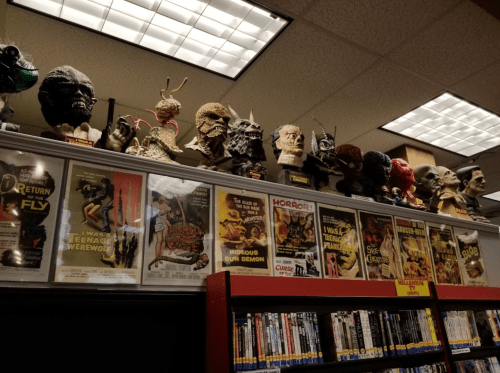 A shelf displaying various monster masks and vintage horror movie posters in a dimly lit room.