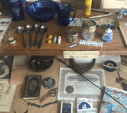 A display case filled with various antique items, including spoons, glassware, and old photographs.