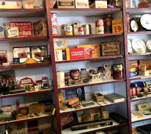A colorful display of vintage boxes, tins, and collectibles on wooden shelves in a nostalgic setting.