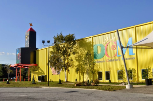 Bright yellow building with colorful signage for a children's museum, featuring a playful design and outdoor play area.