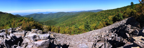 Panoramic view of lush green mountains and rocky terrain under a clear blue sky.