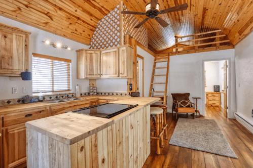Cozy wooden kitchen with a loft, featuring a central island, wooden cabinets, and a warm, rustic atmosphere.