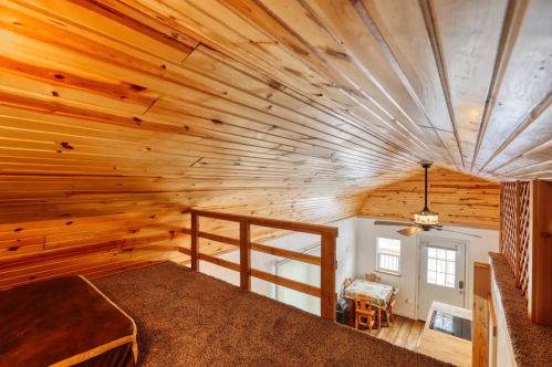 Cozy loft with wooden ceiling, overlooking a dining area and entrance, featuring a ceiling fan and warm lighting.