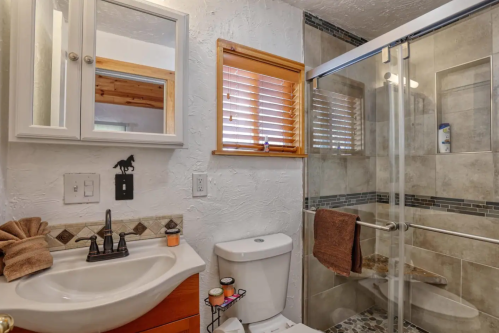 A modern bathroom featuring a shower, sink, and wooden accents, with natural light from a window.
