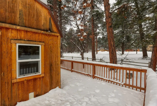 A wooden cabin surrounded by snow-covered trees and a wooden railing, creating a cozy winter scene.