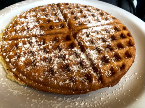 A golden-brown waffle dusted with powdered sugar on a white plate.