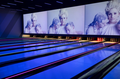 A modern bowling alley with vibrant blue lanes and large screens displaying artistic images.