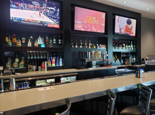 A modern bar with a variety of liquor bottles, three TVs displaying sports and a vibrant atmosphere.