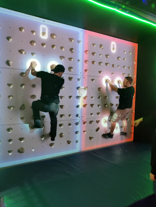 Two people climbing on a brightly lit rock wall with colored sections, focused on reaching the top.