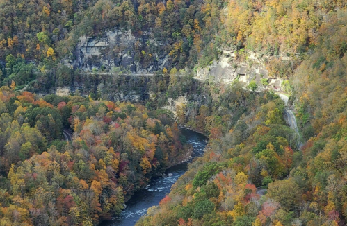 Aerial view of a river winding through vibrant autumn foliage and rocky cliffs.