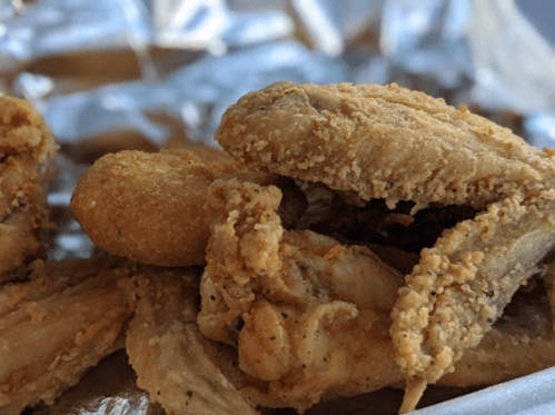 A close-up of crispy fried chicken wings and a fried piece of chicken on a silver tray.