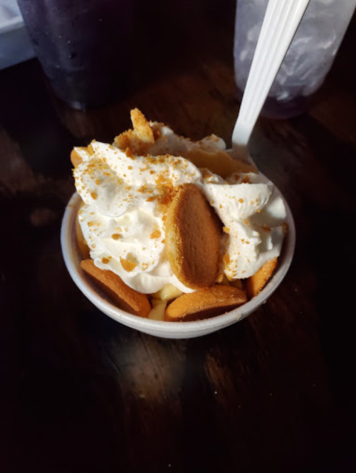 A cup of dessert topped with whipped cream and crushed vanilla wafers.