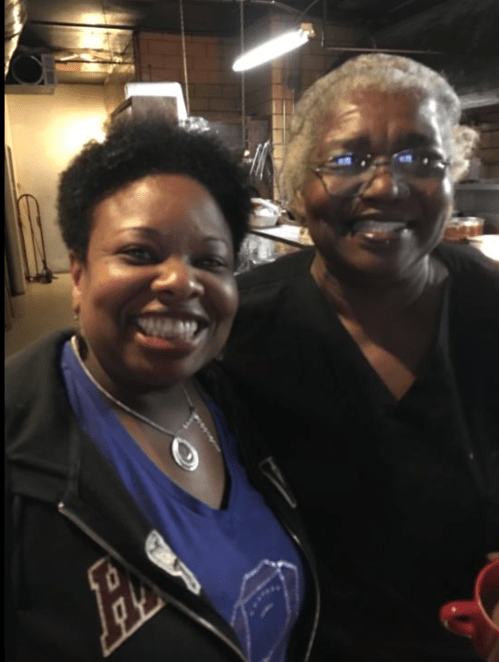Two smiling women pose together in a kitchen setting, showcasing warmth and friendship.